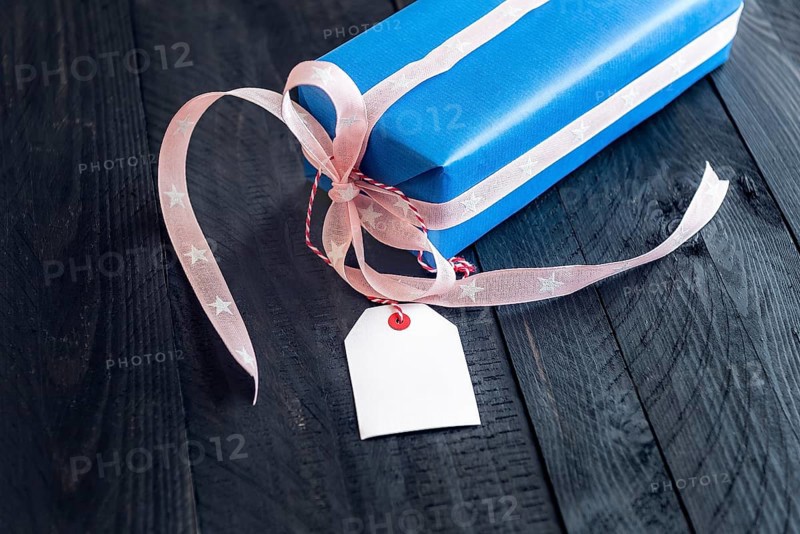 Chic present, wrapped in blue paper and tied with pink ribbon and bow, with an empty label attached to it, on a black wooden table