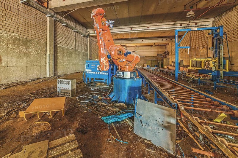 Abandoned factory building with a large orange-coloured robot arm amidst machines and equipment, Metallwerke Bender, Lost Place, Linn, Krefeld, North Rhine-Westphalia, Germany, Europe