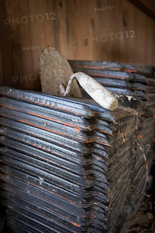Many roof tiles stacked in a barn, on top an old spatula, cobwebs, background wooden wall, Wallonia, Belgium, Europe