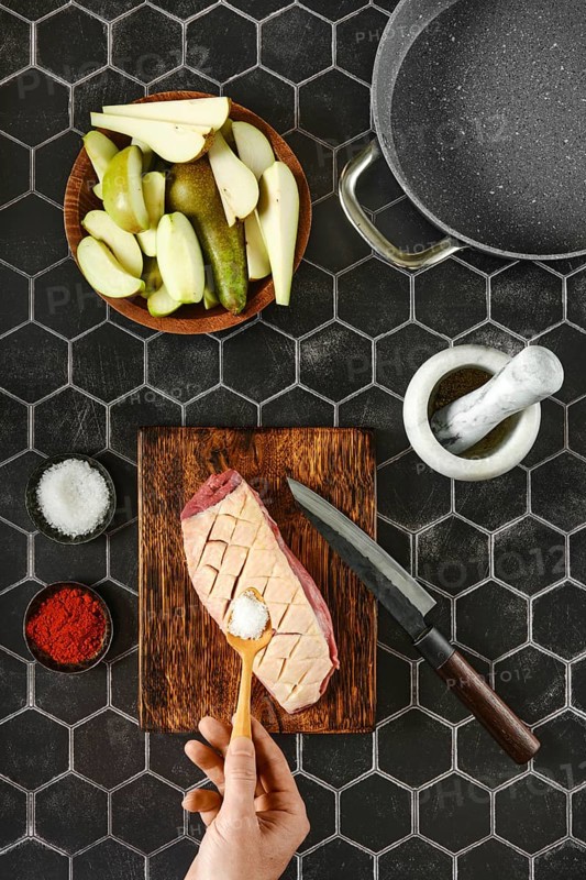 Top view of hand adding salt on raw duck breast with the skin cut crosswise on wooden chopping board