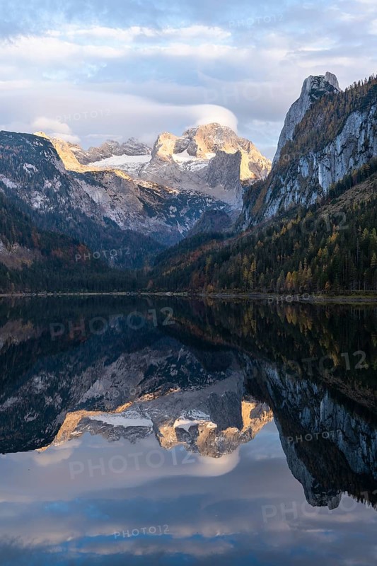 The Vordere Gosausee lake in autumn with a view of the Dachstein mountain range. The Gosaukamm on the right. Clouds in the blue sky and above the mountain peak. Reflection. Golden hour. Vorderer Gosausee, Gosau, Gosau valley, Salzkammergut, Upper Austria, Austria, Europe