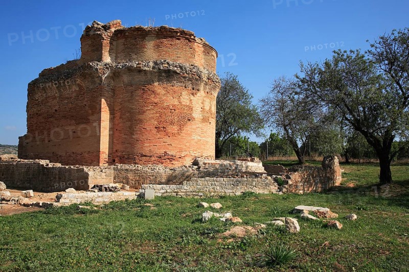 Roman ruins of Milreu, near Estoi, Algarve, Portugal, Old round brick wall, surrounded by trees and meadow, under a clear blue sky, Europe