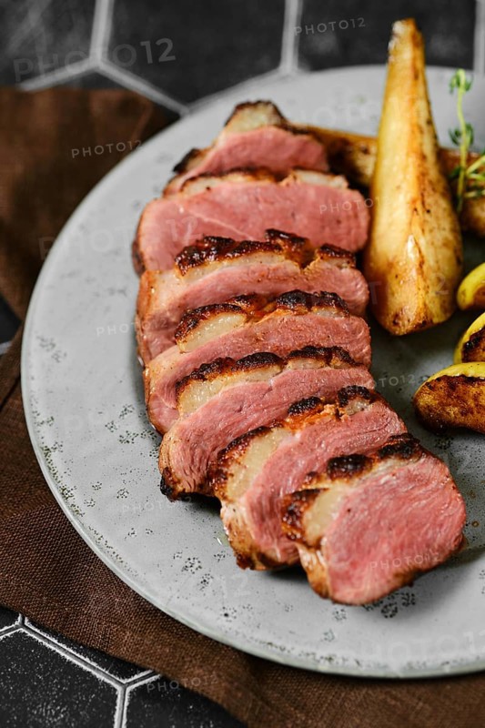 Close-up view of seared duck breast with golden-brown roasted potato wedges
