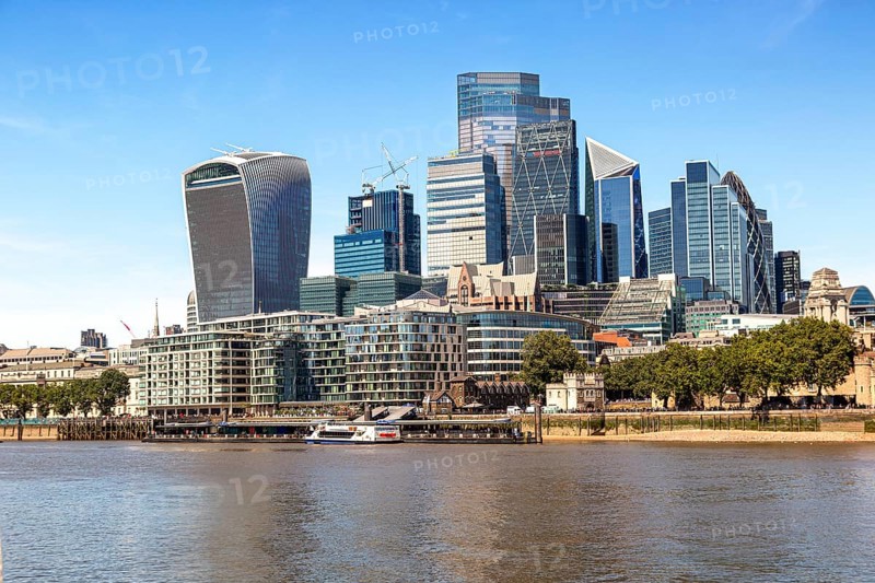 Modern skyline with tall glass buildings along the River Thames and trees in the foreground, London, United Kingdom, Europe