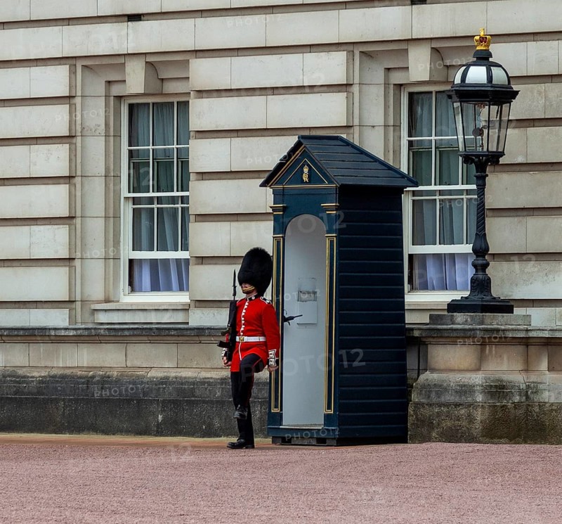 A guard in red uniform stands in front of a sentry box next to a lantern at Buckingham Palace, London, United Kingdom, Europe