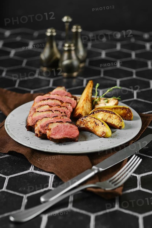 A succulent duck breast is perfectly seared and surrounded by tender, caramelized apple and pear slices in a plate