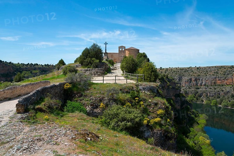 A picturesque church stands on a lush hill with a path, under a bright blue sky in a vast landscape, Ermita de San Frutos, Natural Park of the Gorges of the Duratón River, Duraton, Parque Natural de las Hoces del Río Duratón, Sepulveda, Segovia, Valladolid, Castilla y León, Spain, Europe