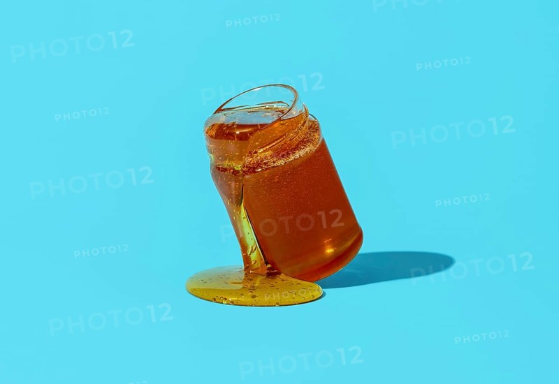 Jar with honey minimalist on a blue table. Dripping honey from a glass jar directly on the table