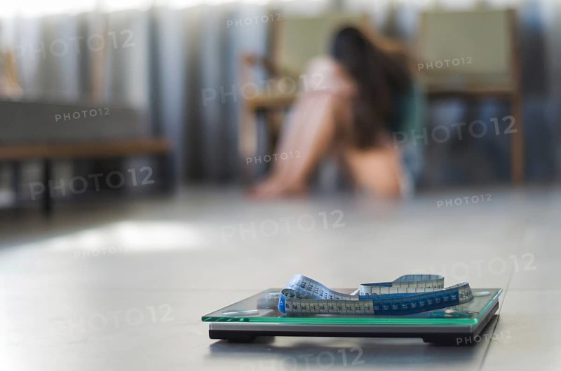 Concept of failing in weight loss, scales in the foreground and frustrated frustrated woman in the background