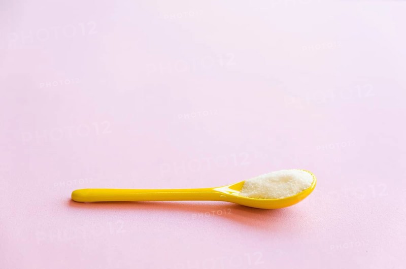 Spoon with sugar close-up on a pink background