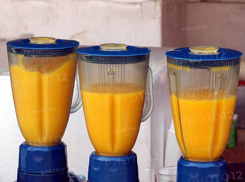 Three electric blenders are making fresh mango smoothies
