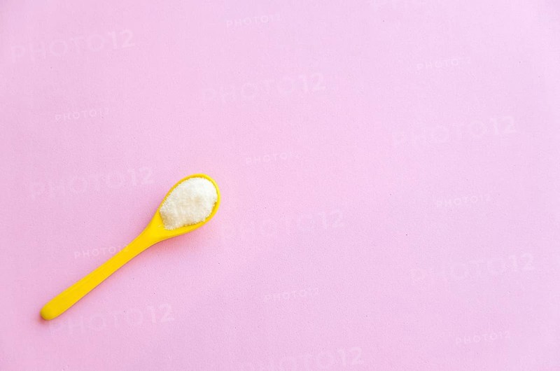 Spoon with sugar close-up on a pink background