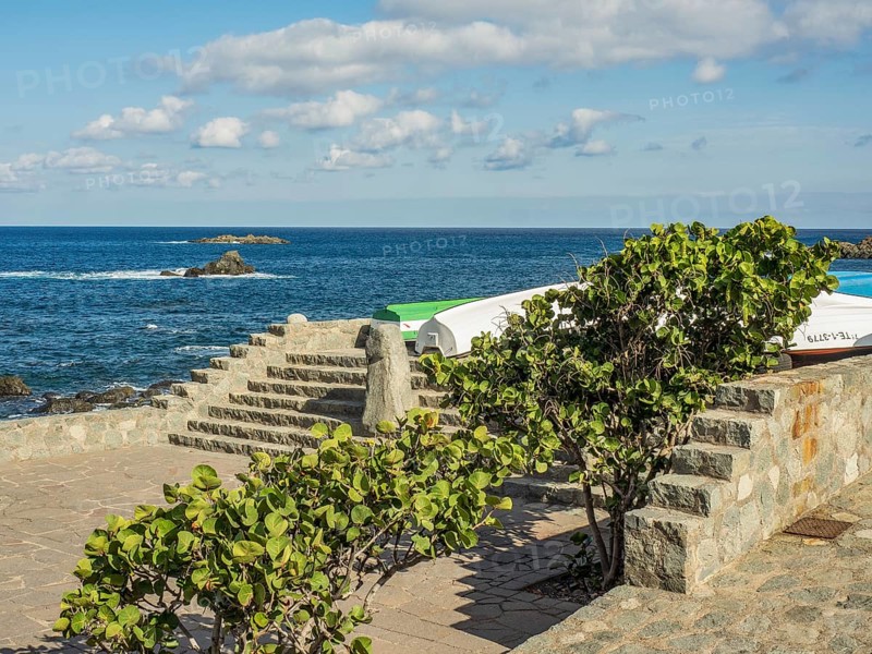 Stone steps at the edge of the ocean with boats, plants and clouds in the sky, tenerife, canary islands, spain