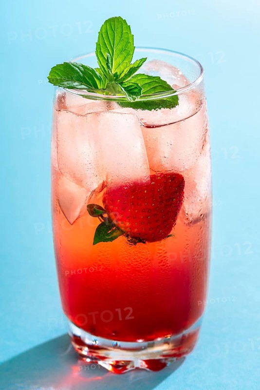 Glass of strawberry drink with ice cubes and mint leaves on a seamless blue background. A single glass of fruity cocktail. Summer sweet drink