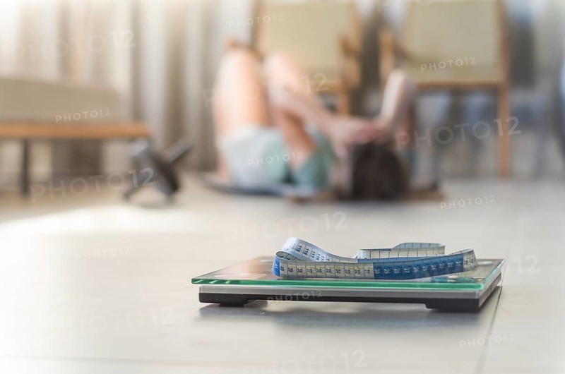 Concept of failing in weight loss, scales in the foreground and frustrated frustrated woman in the background