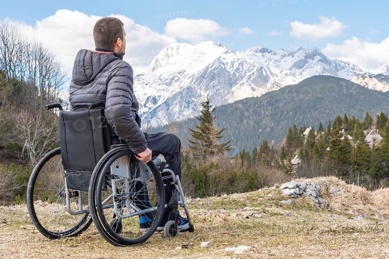 Photo of Young disabled man in wheelchair outside in nature observing mountains and nature