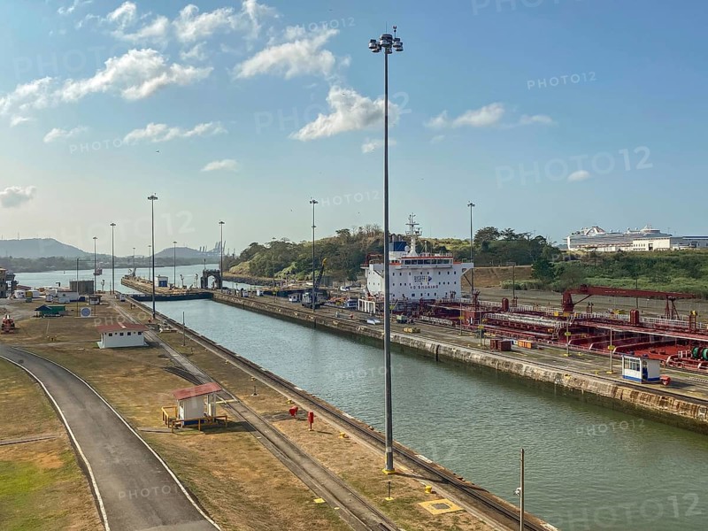 A ship moves through a canal surrounded by streets and lampposts. The atmosphere is calm and the sky is clear, panama city, panamakanl, panama, Central America
