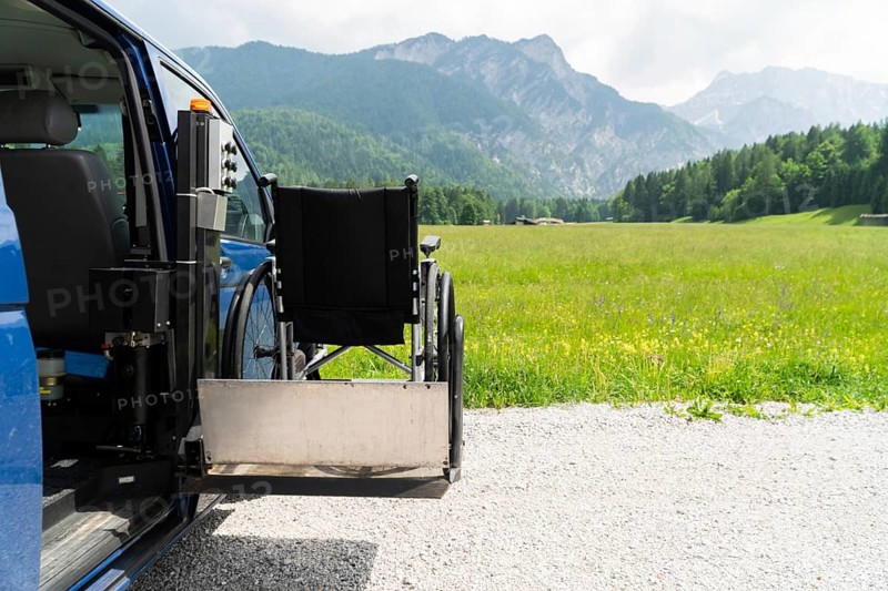 Photo of black electric lift specialized vehicle for people with disabilities. Empty wheelchair on a ramp with nature and mountains in the back