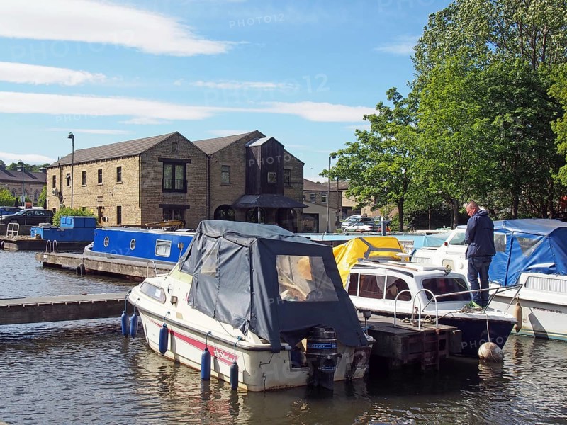 Brighouse, west yorkshire, united kingdom: 24 may 2017: a man on a houseboat surrounded by barges moored in the brighouse basin and moorings on the calder and hebble navigation canal in calderdale west yorkshire