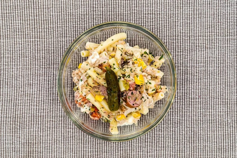 Pasta salad dish with corn, tuna and a pickle on a gray background