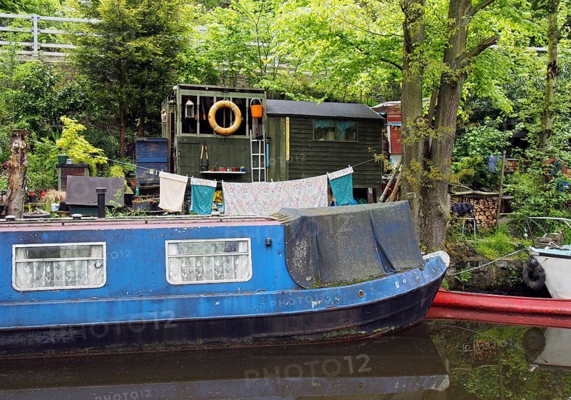 An old scruffy blue narrow boat moored next to wooden sheds with washing on the line on the rochdale canal near hebden bridge