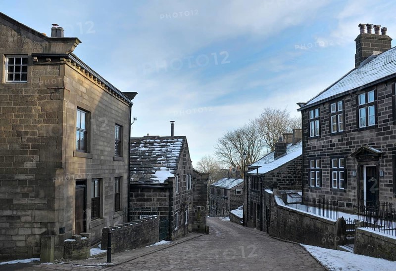 View of the main street in the village of Heptonstall in west Yorkshire with snow on roofs with blue winter sky