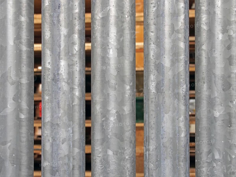A close up of vertical galvanized steel fence with wooden pallets in outdoor storage visible between the gaps