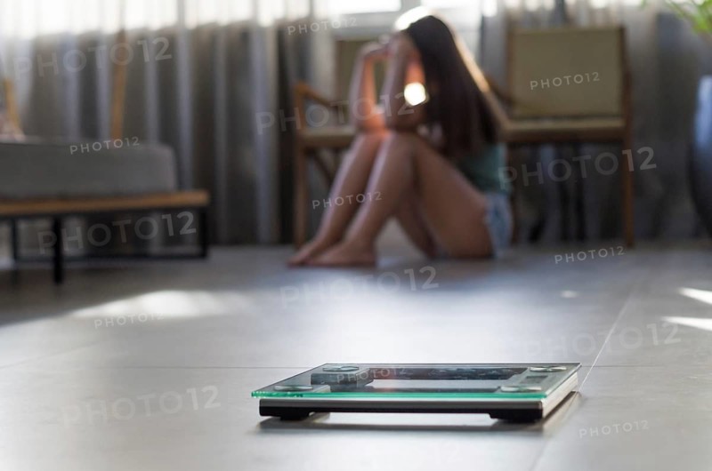 Concept of failing in weight loss, scales in the foreground and frustrated frustrated woman in the background