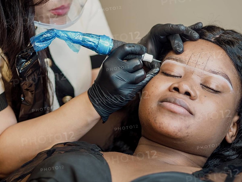 Person relaxing while a professional in gloves performs permanent tatoo on their eyebrows with careful precision