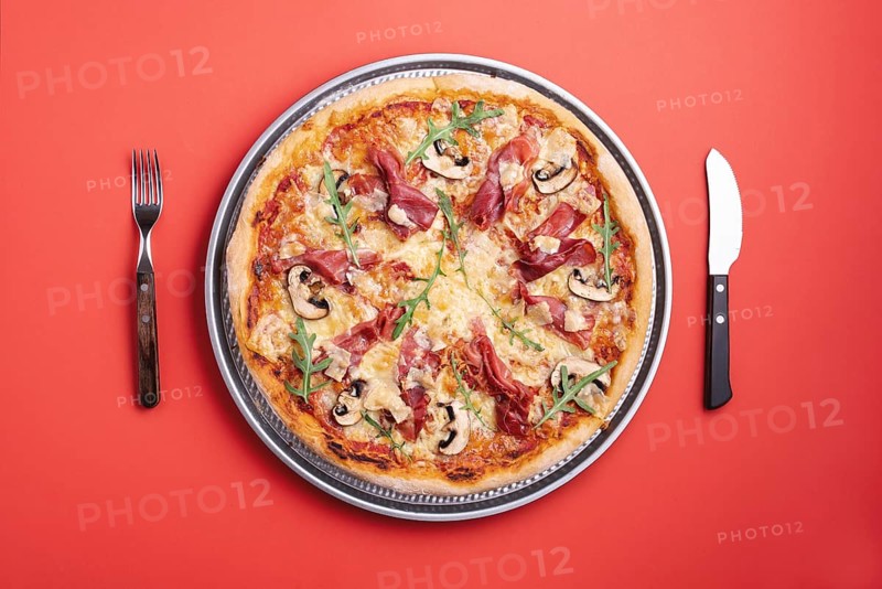 Homemade pizza with prosciutto crudo, arugula, mozzarella and champignons. Flat lay with a ham pizza ready to eat. Prosciutto and arugula pizza top view