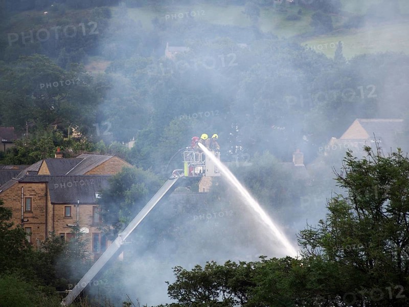 Hebden bridge, west yorkshire, united kingdom, 1 august 2019: firemen on an elevated platform putting out the fire at the former walkeys clogs mill in hebden bridge