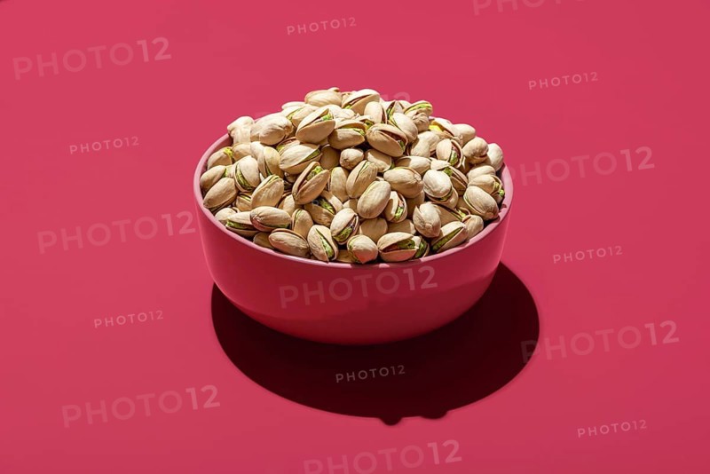 Pink bowl with roasted and salted pistachio minimalist on a magenta table. Bowl with pistachio isolated on a vibrant-colored background