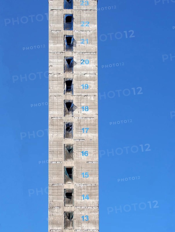 A tall concrete structure and service core of a new skyscraper building under construction with floor numbers marked in paint against a blue sky
