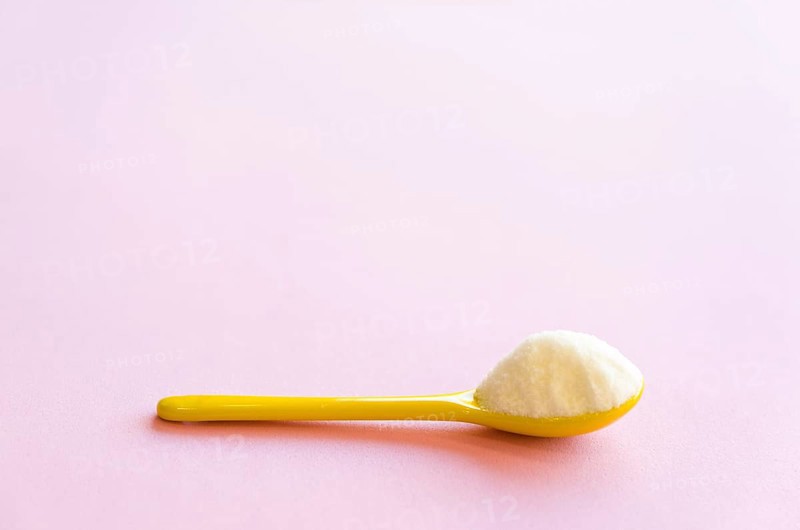 Spoon with sugar close-up on a pink background