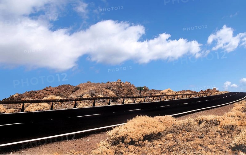 Empty two lane black road stretching to the horizon in desert scrub with blue sky and white lane markings