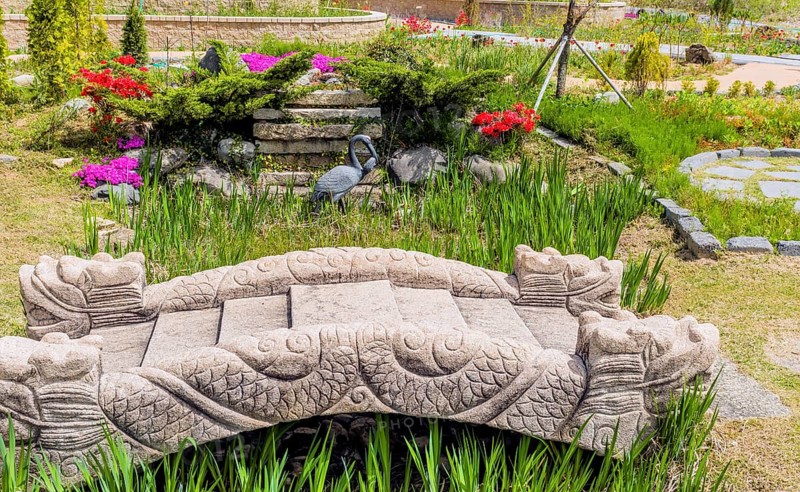 A stone bridge adorned with sculptures amidst plants and flowers in a colorful garden in Gyeongju, South Korea, Asia