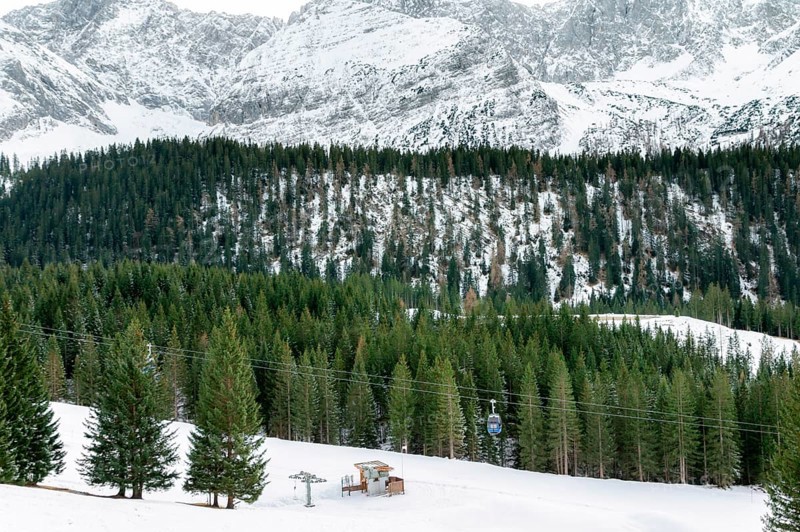 Curved foothills and the rocky Alps mountains covered by snow and green fir trees, a cableway system, in Ehrwald, Austria, in December, Europe