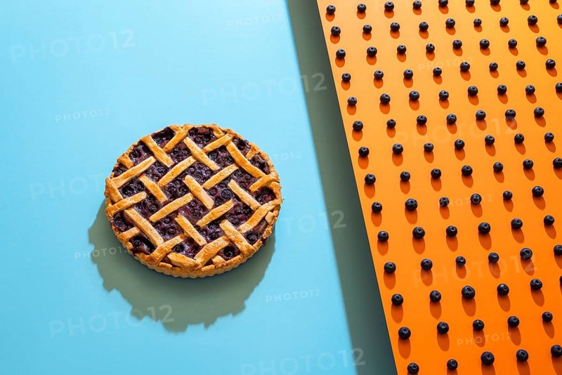 Classic blueberry pie with lattice crust on blue background and blueberries pattern on orange background. A berry pie and the main ingredient