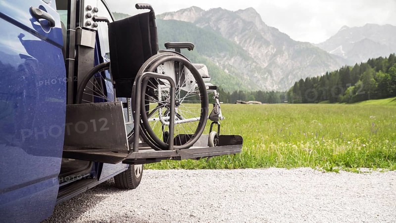 Photo of black electric lift specialized vehicle for people with disabilities. Empty wheelchair on a ramp with nature and mountains in the back