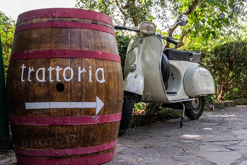An antique wine barrel and a Vespa scooter at the entrance of a trattoria in Tuscany