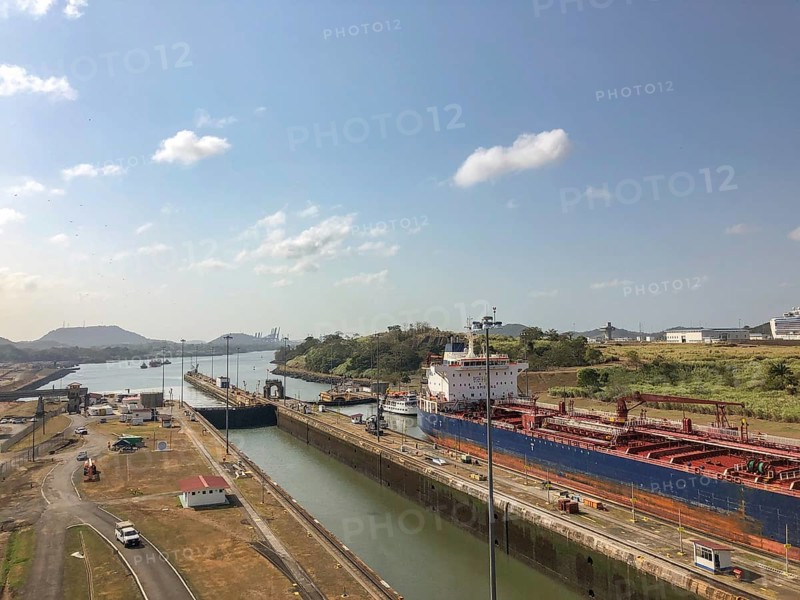 A tranquil canal scene with a large ship and buildings, the surrounding landscape is structured and the sky clear, panama city, panamakanl, panama, Central America