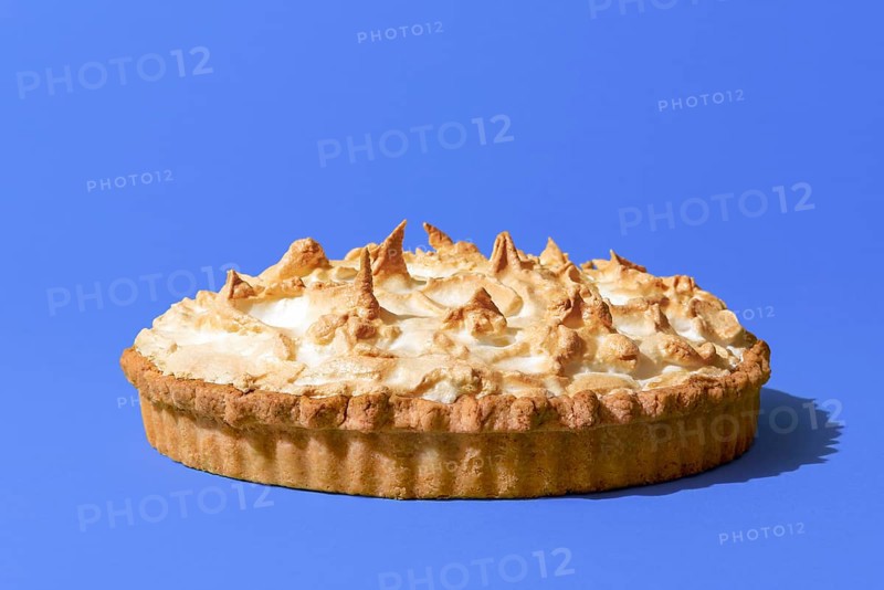 Delicious homemade meringue cake with a lemon flavor filling, minimalist on a blue indigo table. Lemon meringue tart isolated on a vibrant colored background
