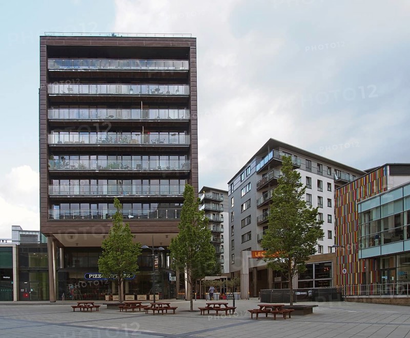 Leeds, west yorkshire, united kingdom, 16 july 2019: bars restaurants and modern apartment buildings in the leeds dock area around a public square with trees and benches