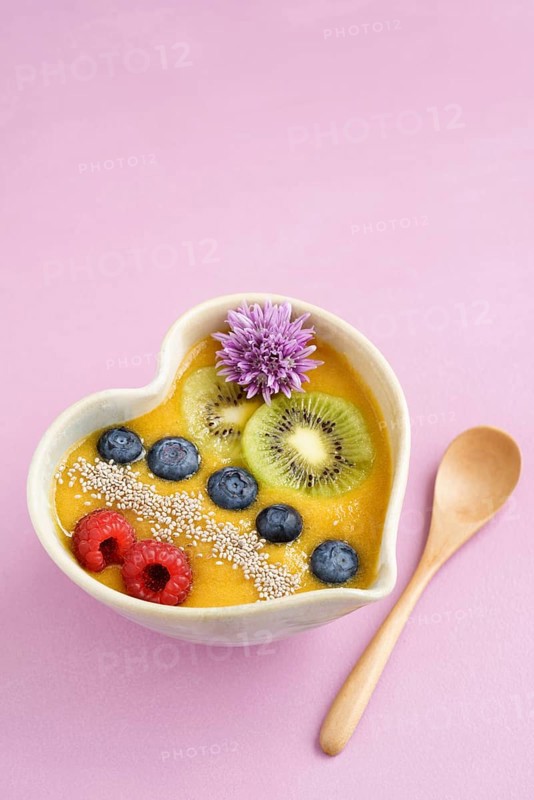 Peach smoothie bowl with blueberries, kiwi, white chia seeds and raspberries in a heart shaped bowl
