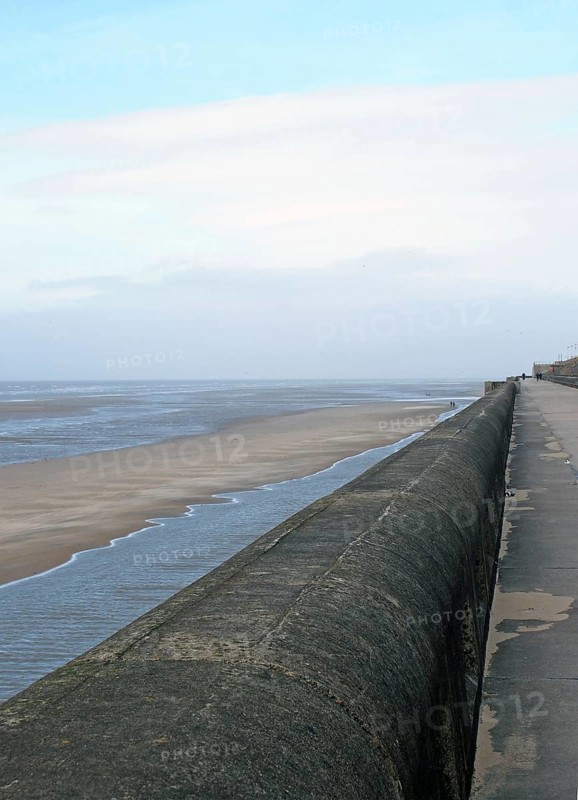Perspective view of the seawall in blackpool with the beach at low tide in sunlight with the beach and sea