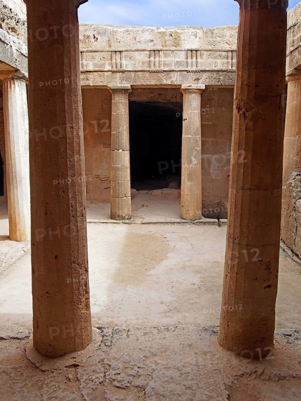 An underground chamber at the tombs of the kings in paphos cyprus with old eroded sandstone columns surrounding a dark empty doorway and blue sky