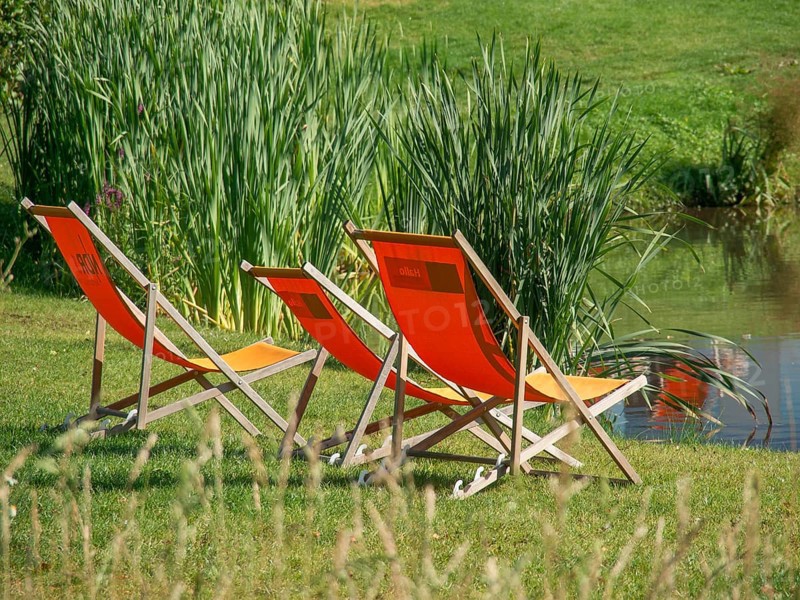 Three orange deckchairs on the banks of a pond in summer, papenburg, emsland, germany