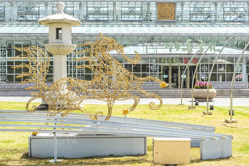 A golden sculpture of a horse next to a lantern in front of a building with a glass facade in Gyeongju, South Korea, Asia