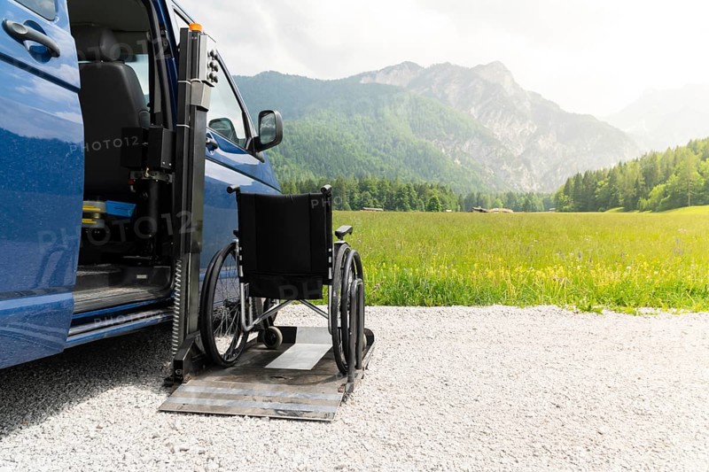 Photo of black electric lift specialized vehicle for people with disabilities. Empty wheelchair on a ramp with nature and mountains in the back
