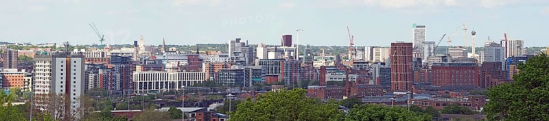 A wide panoramic view showing the whole of leeds city center with towers apartments roads and commercial buildings against a blue sky